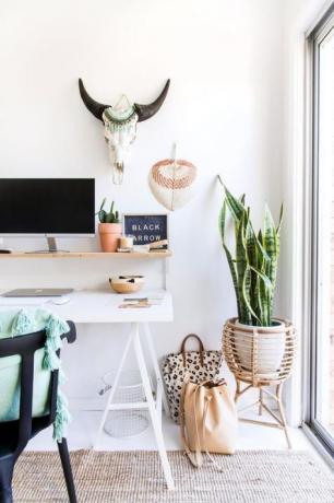 Área de trabalho com uma mesa branca atraente, cadeira de vime, macramê e plantas domésticas